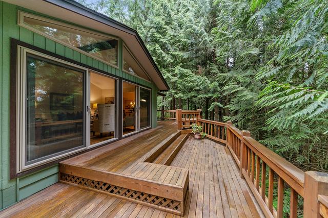 A wide natural-wood deck with railings and built-in steps along the side of a green house