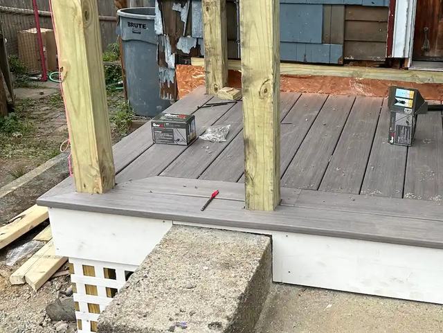 A small gray composite-board porch deck under construction, with new pressure-treated posts