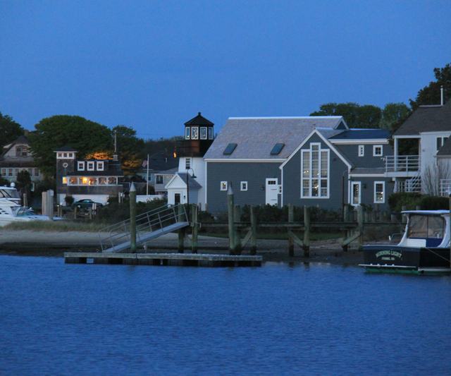 Gray-shingled New England houses along a harbor at dusk